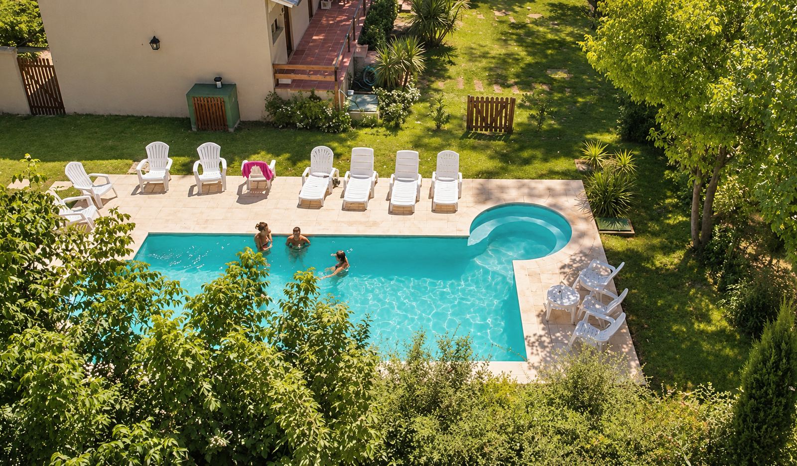 La pileta de Monserrat Bungalows con reposeras blancas y los bungalows detrás, entre árboles